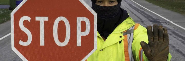 A man wearing a mask is standing in front of a stop sign.