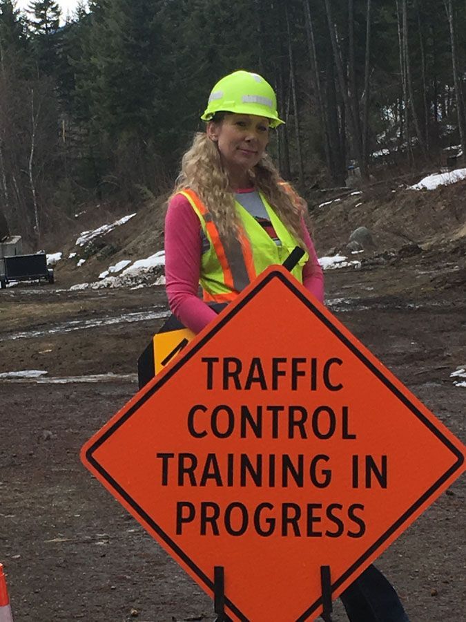 A woman in a hard hat is holding a traffic control training in progress sign
