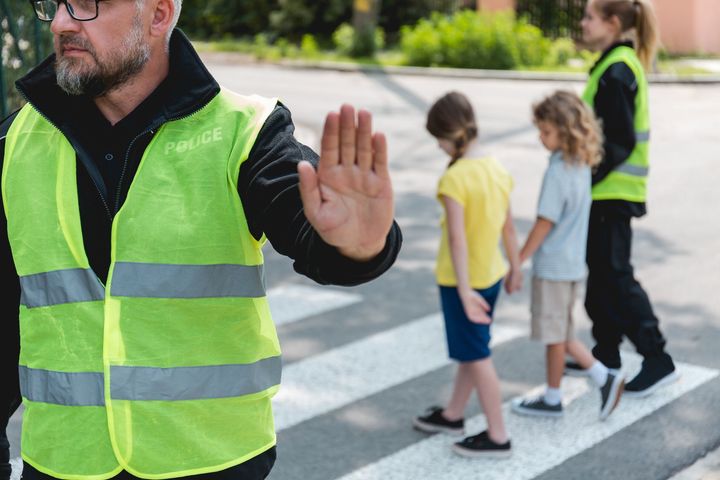 A man in a yellow vest is giving a stop sign to children crossing the street.