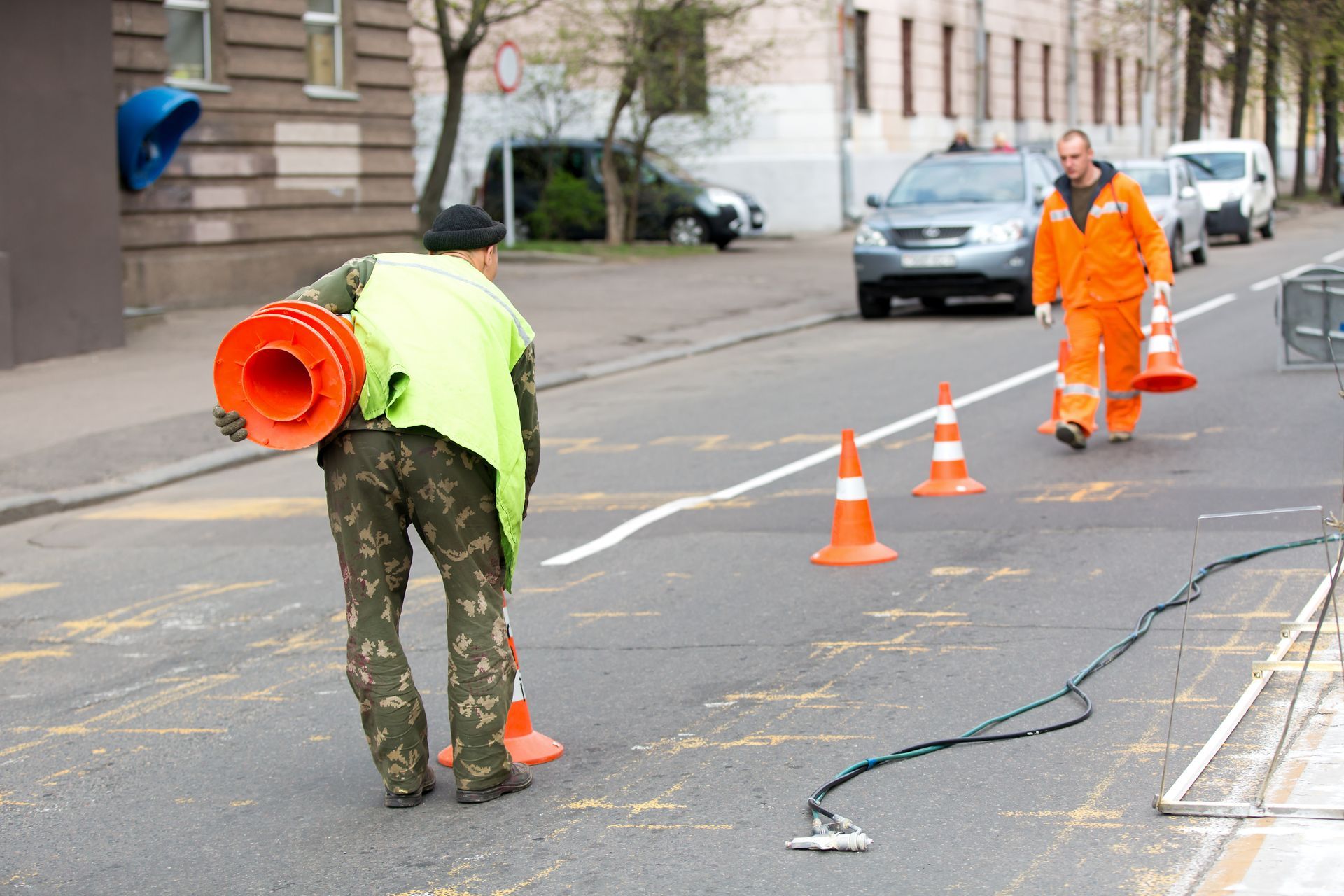 A man in a yellow vest is carrying an orange cone on his back.