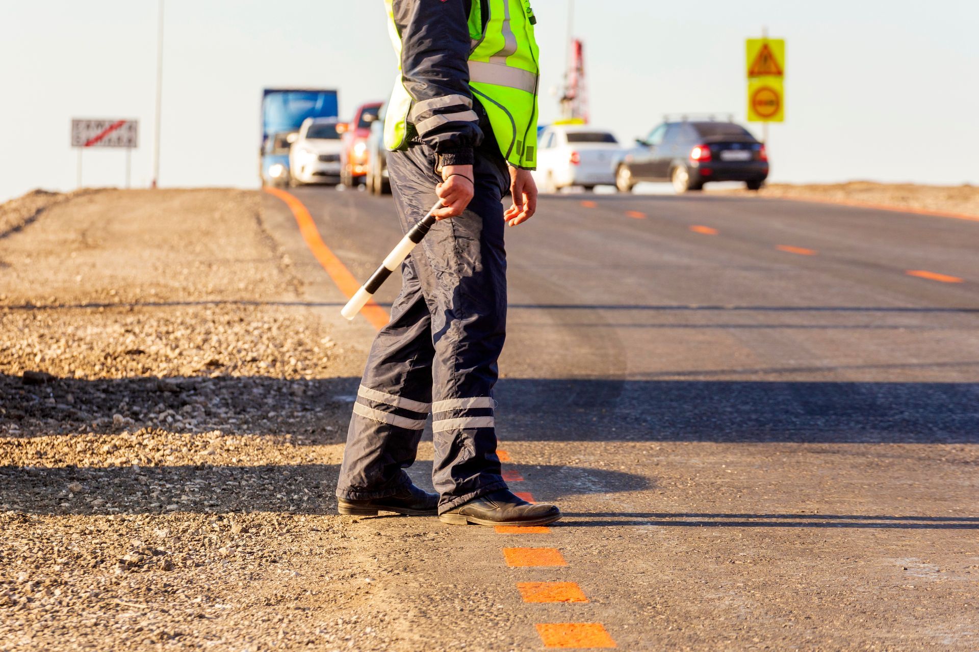 A man is standing on the side of the road holding a traffic cone.