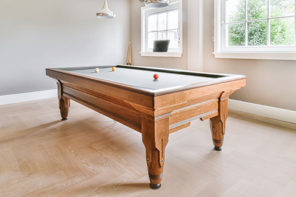 A pool table is sitting in a room next to a window.