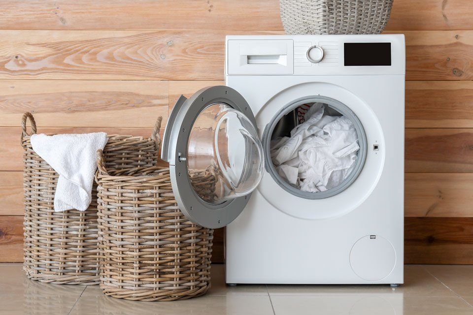 A washing machine is filled with white clothes next to two wicker baskets.