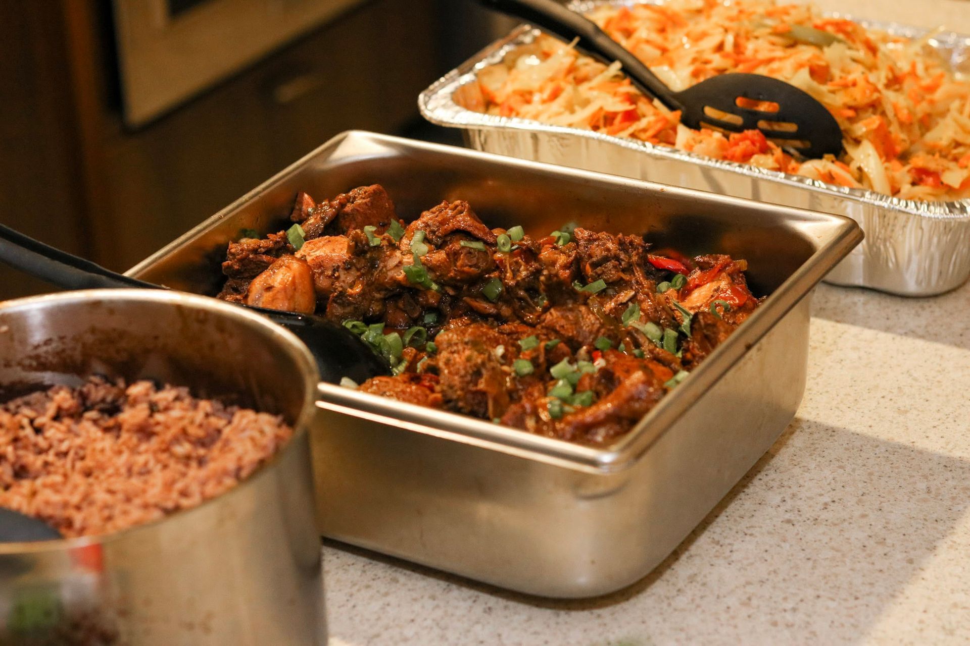 Food buffet with metal trays: stew, rice, and slaw.