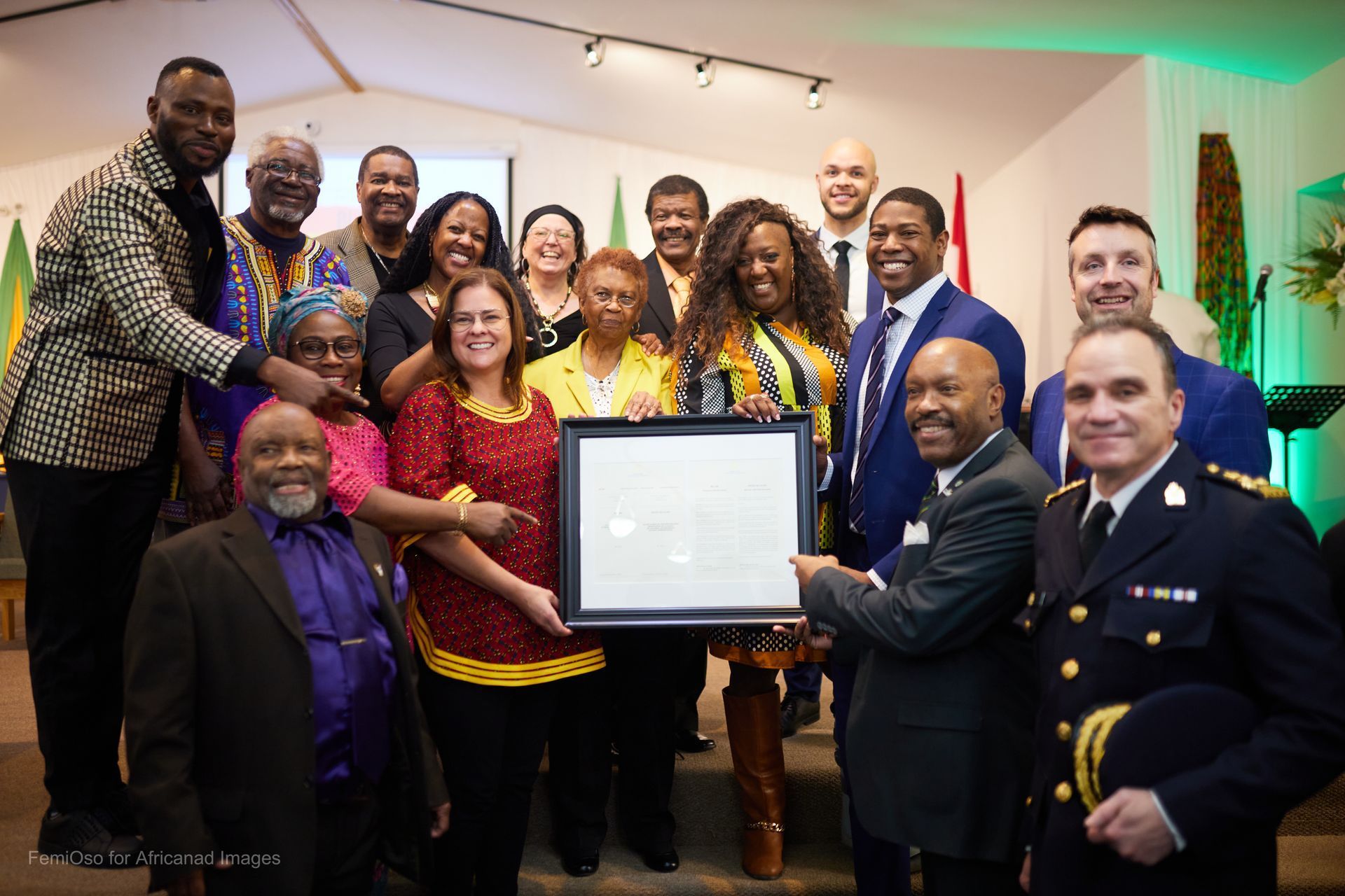 Group of people holding a framed document, some smiling, in a room with flags.