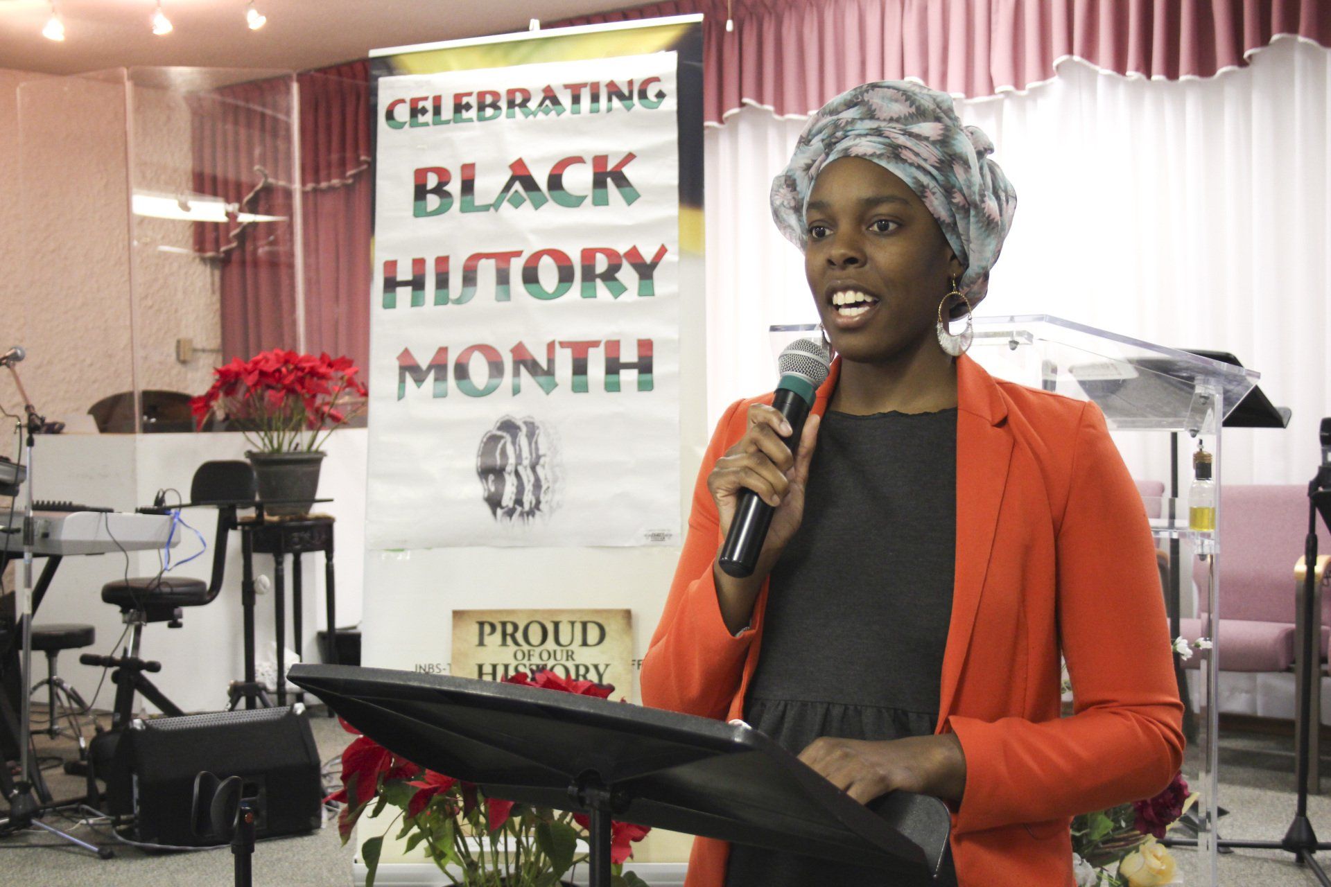 Woman speaking into a microphone at a Black History Month event. Banner in background.