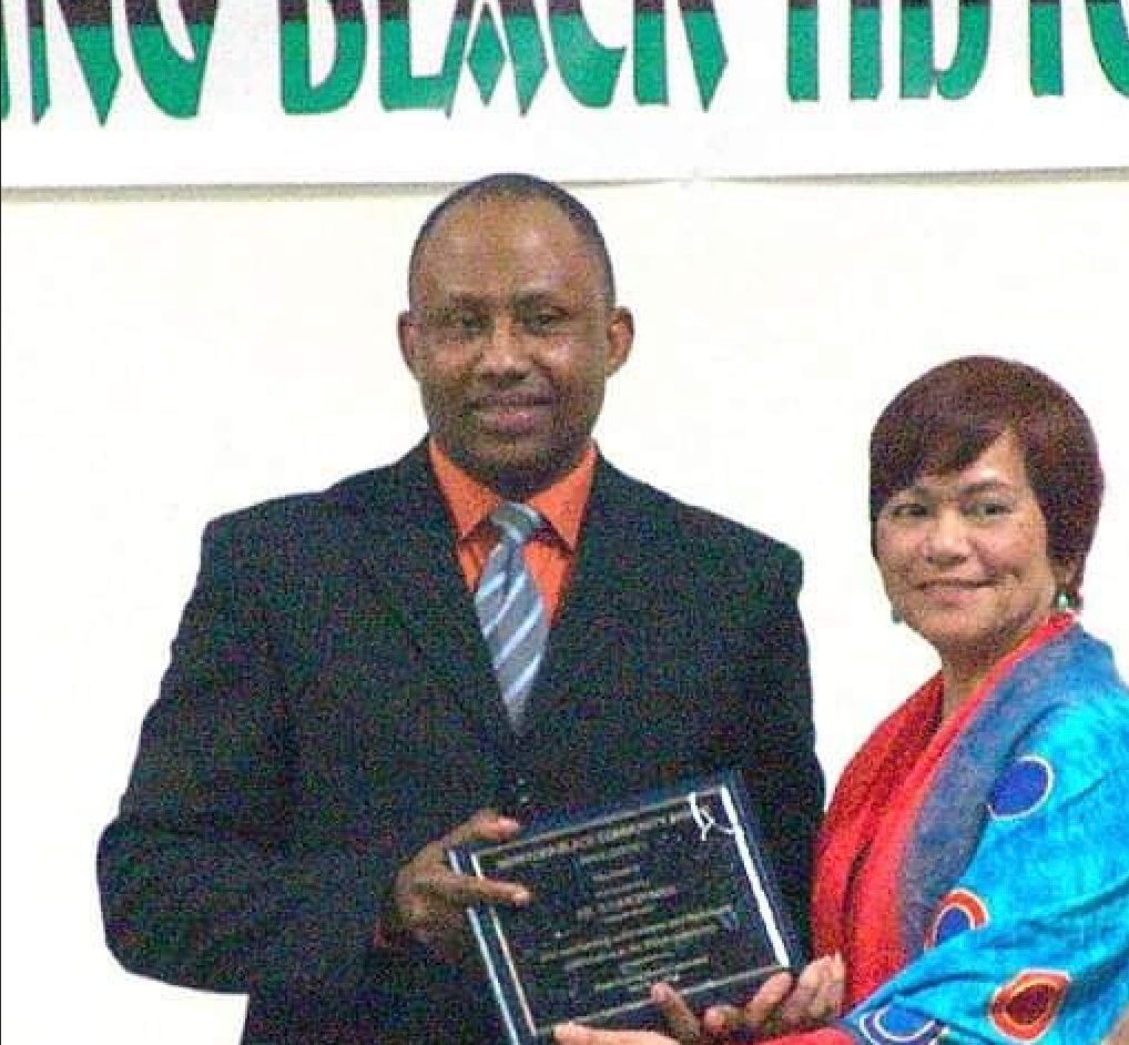 Man in suit accepts a plaque from woman in red and blue, likely an award ceremony.