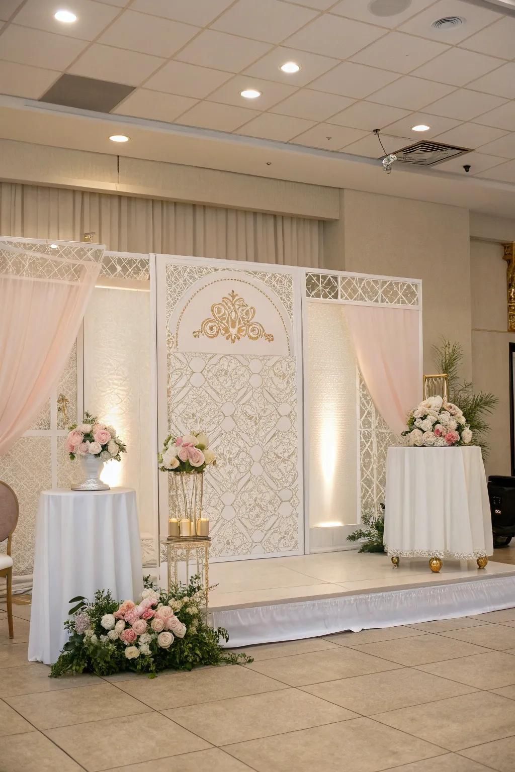 Elegant wedding stage with white floral backdrop, draped curtains, and pink floral arrangements on pedestals