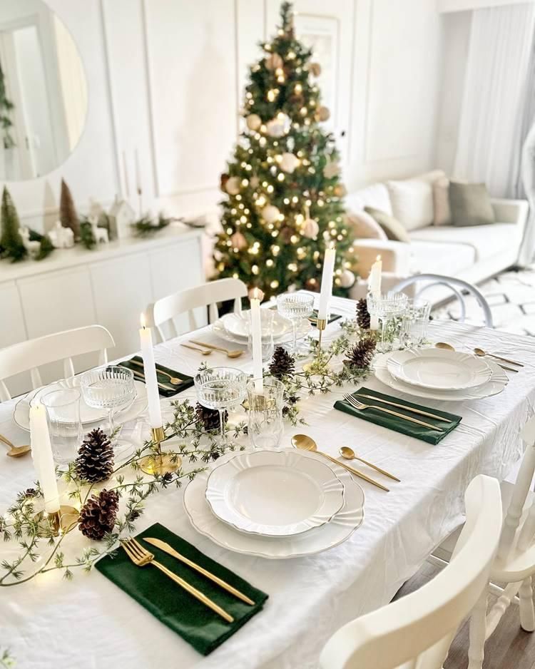 Festive dining table set with white dishes, green napkins, and a decorated Christmas tree behind it
