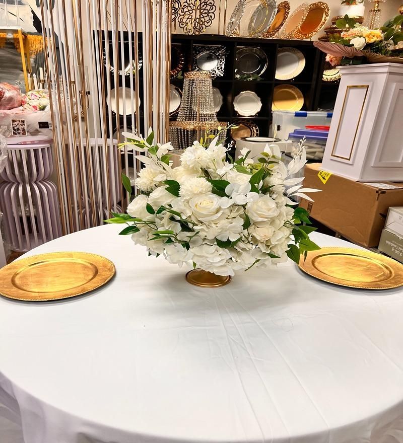 Round white table with gold chargers and a white floral centerpiece in a decorated event hall