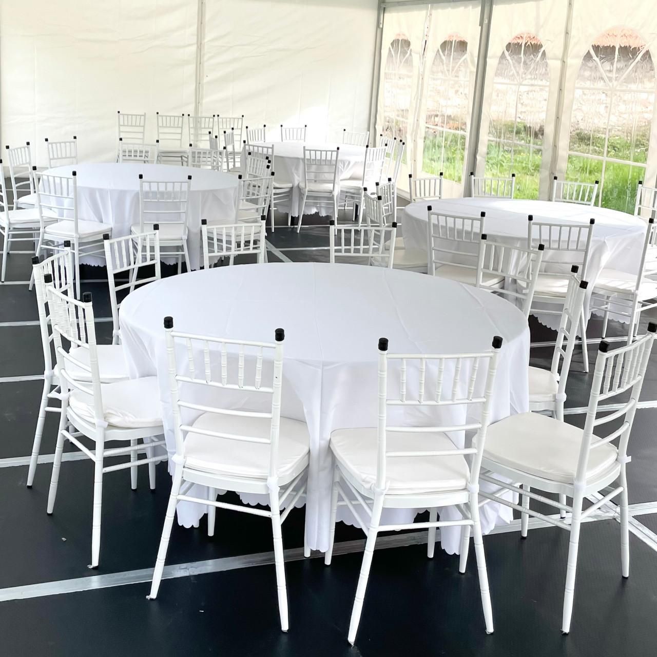 White chairs around round banquet tables inside a bright outdoor event tent.