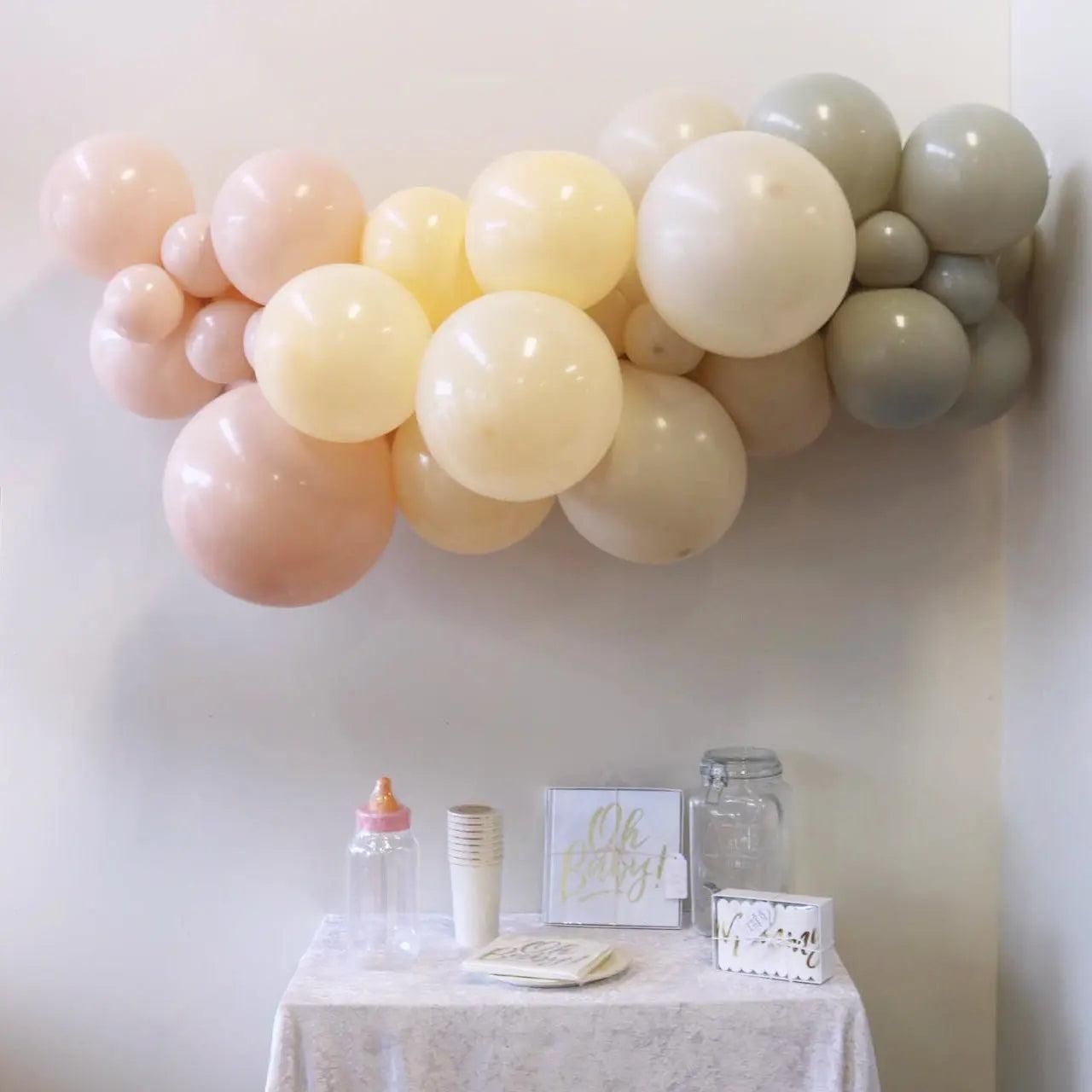 Pastel balloon garland in pink, cream, yellow, and gray above a decorated dessert table