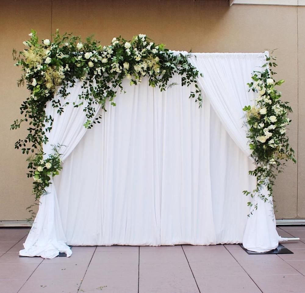 White draped wedding arch with lush green and white floral arrangements at an outdoor venue