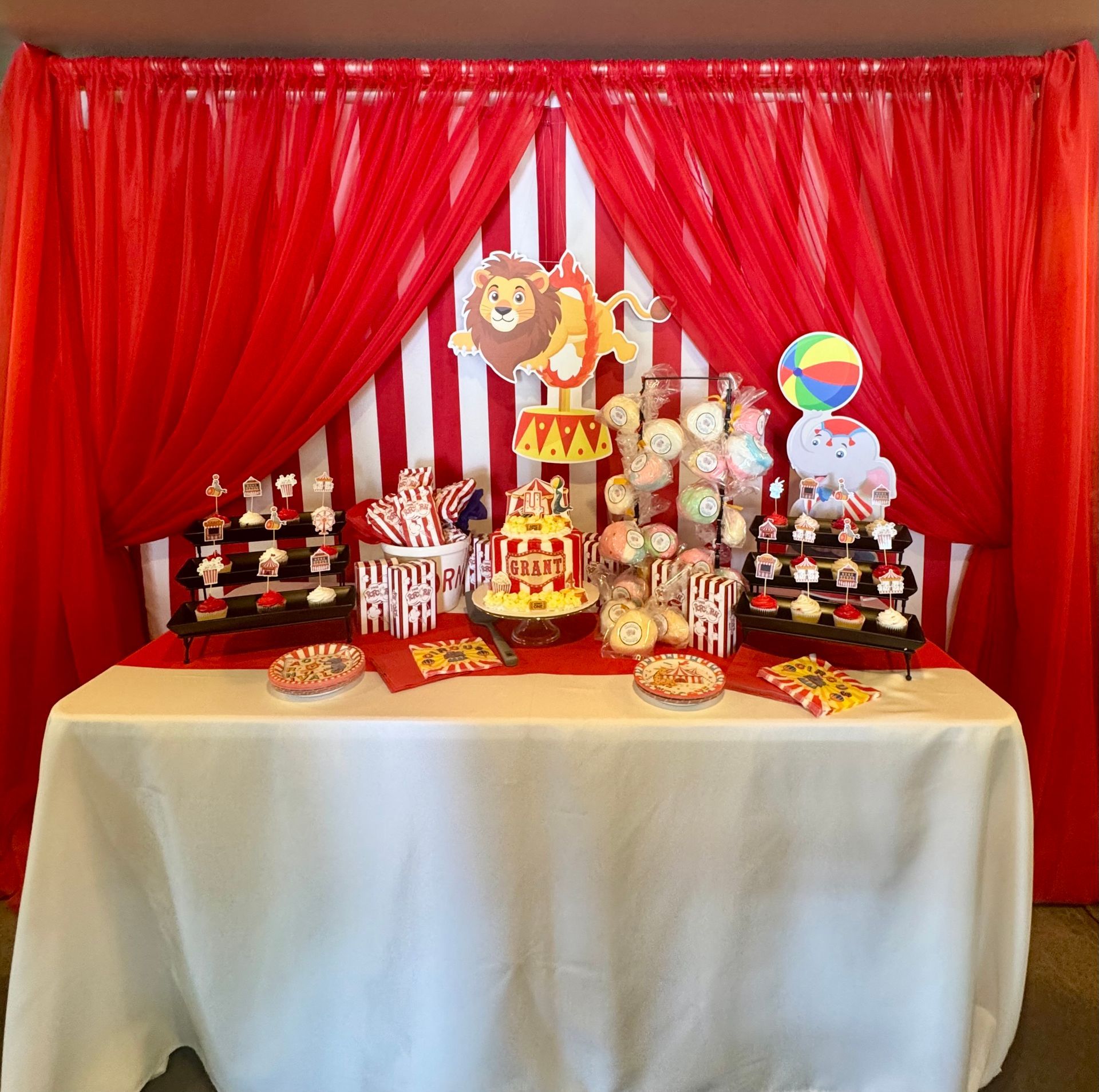 Circus-themed dessert table with red drapes, lion topper, colorful treats, and party decorations