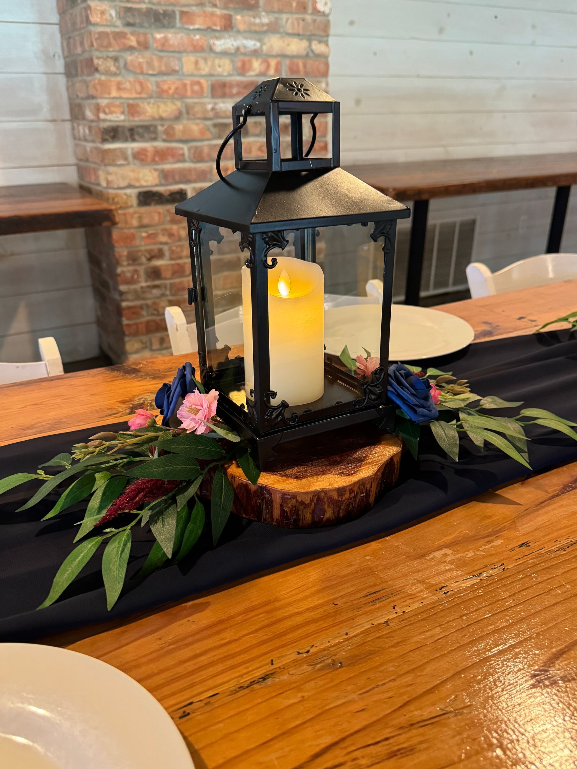 Black lantern centerpiece with candle and flowers on a wooden table setting