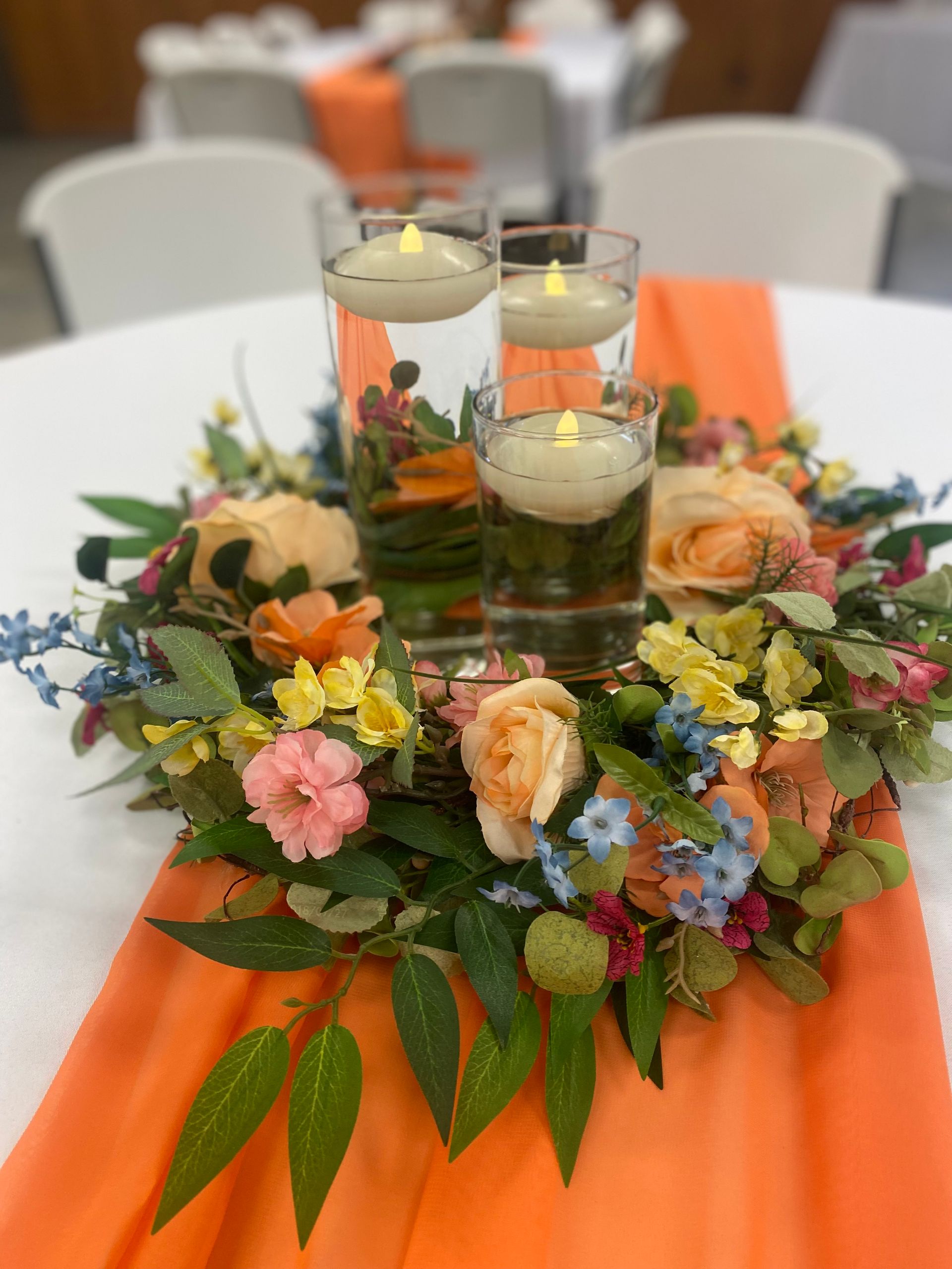 Floral table centerpiece with candles on an orange runner at a banquet table
