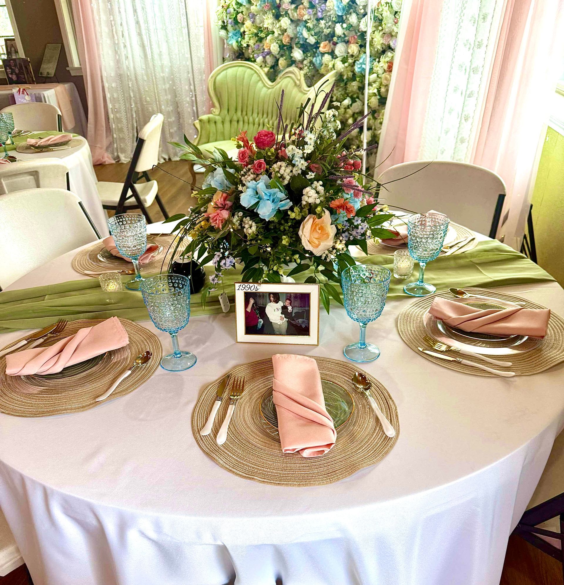 Round banquet table set with white cloth, pink napkins, blue goblets, and a floral centerpiece.