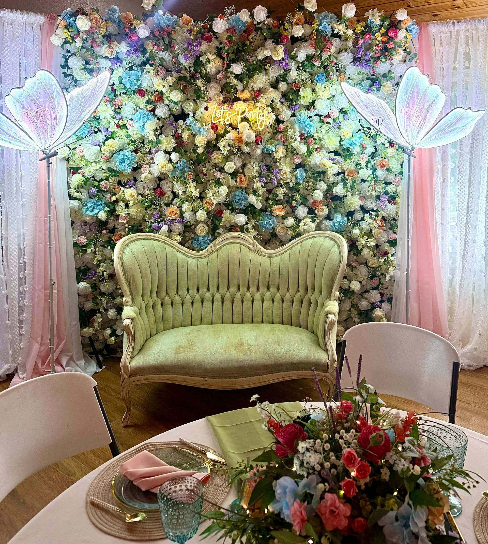 Floral backdrop with a pale green loveseat and decorated table in a pink draped event space
