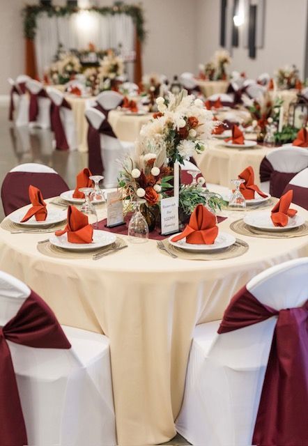 Elegant banquet tables set with cream tablecloths, burgundy chair sashes, and floral centerpieces in a reception hall