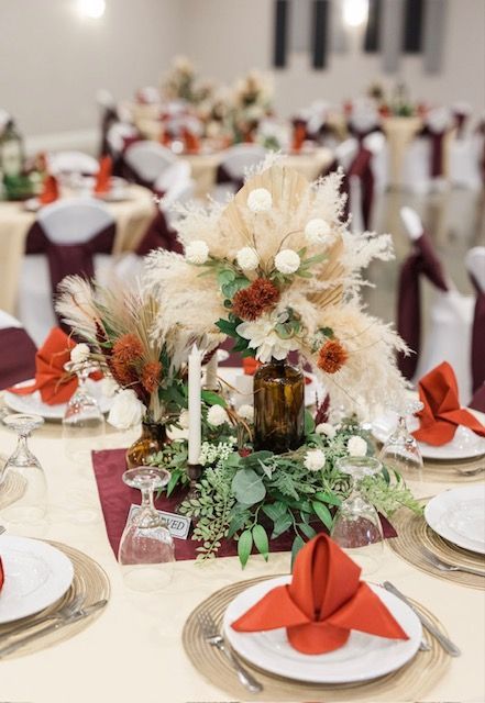 Decorated banquet table with white linens, red napkins, and a floral centerpiece with candles and greenery
