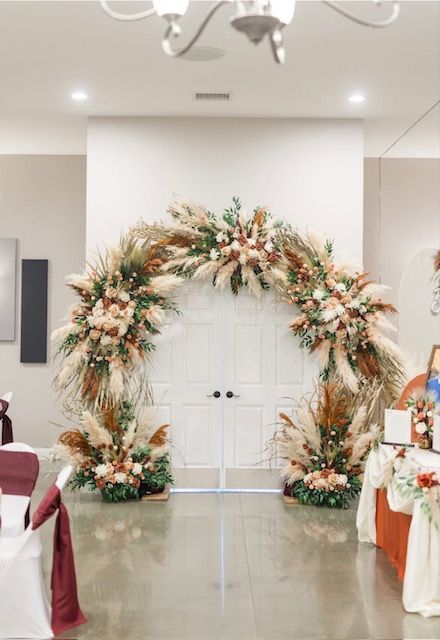Floral wedding arch with white draping and peach-green arrangements in a decorated banquet hall.