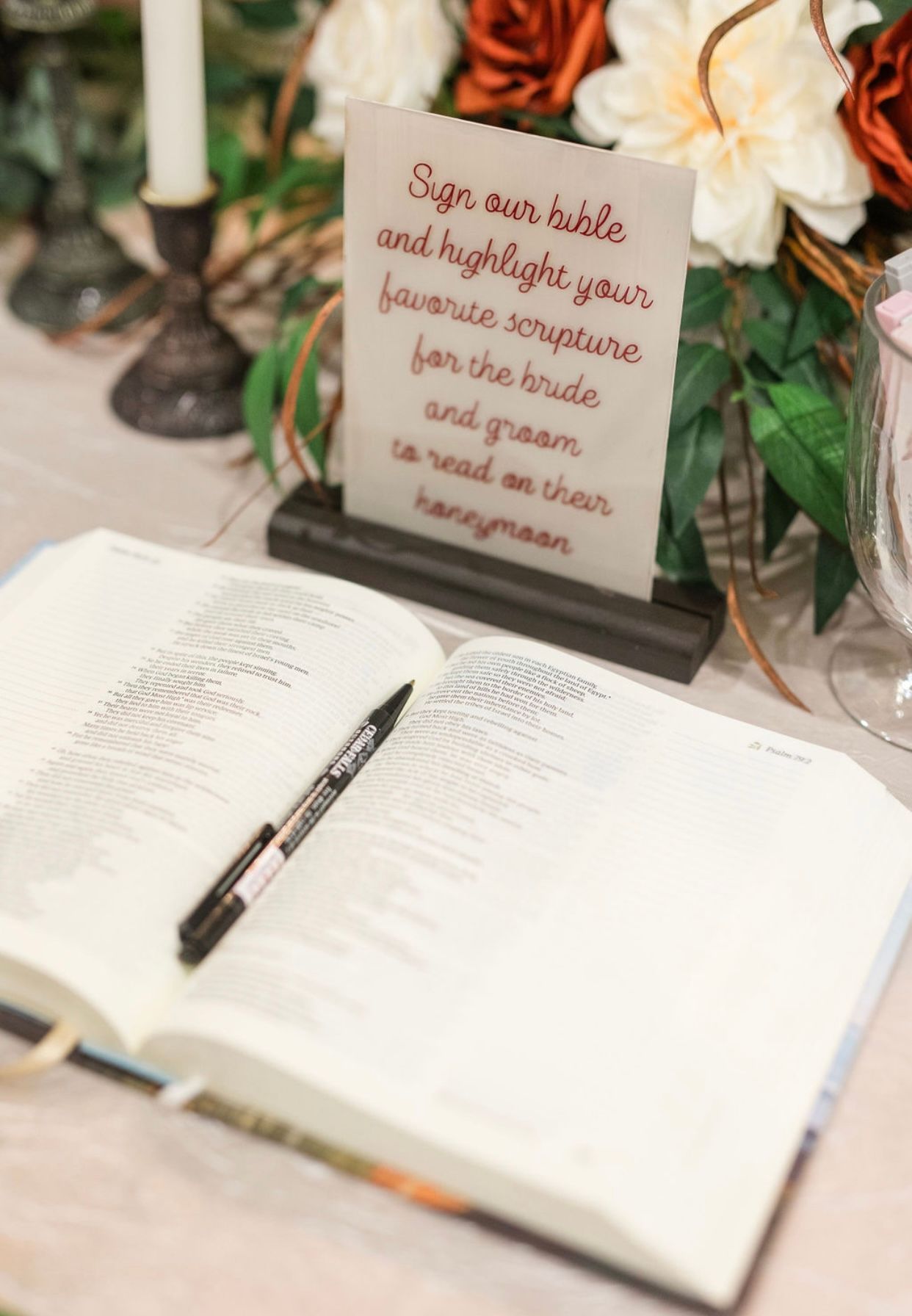 Open wedding guestbook with black pen beside a framed sign and floral arrangement