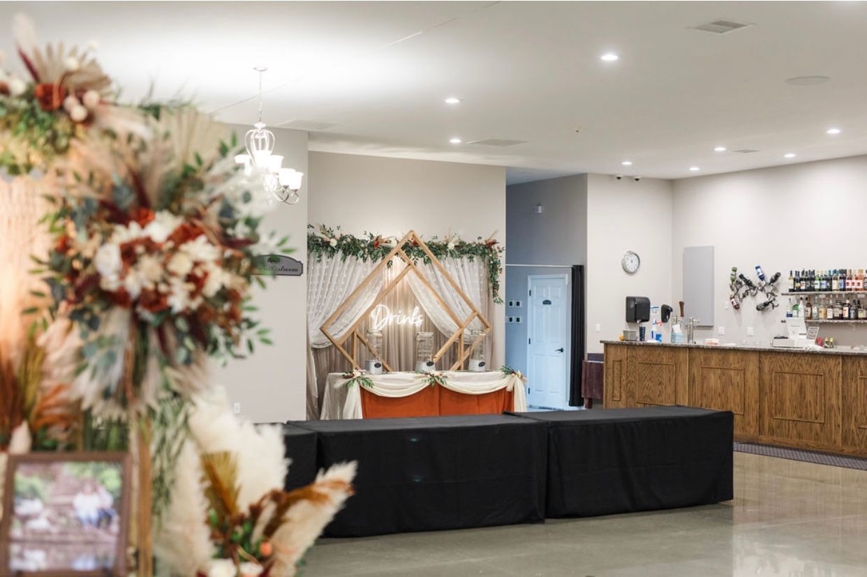 Decorated event venue with floral arrangements, draped backdrop, and black-draped tables beside a wooden reception counter