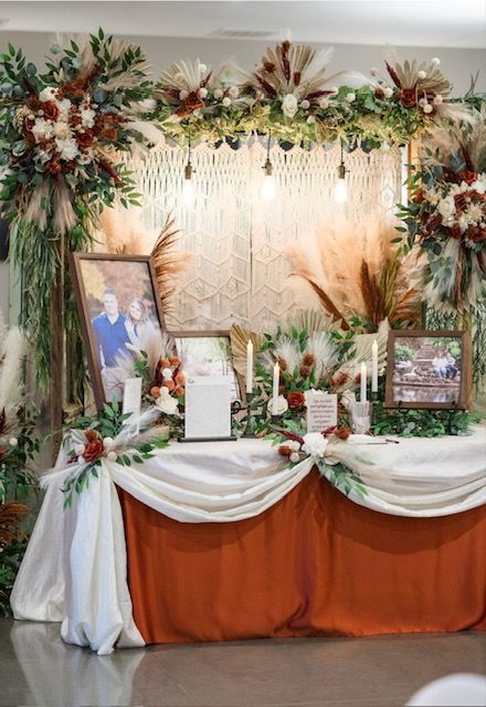 Floral memorial altar with framed photos, candles, and white drapery against a cream backdrop