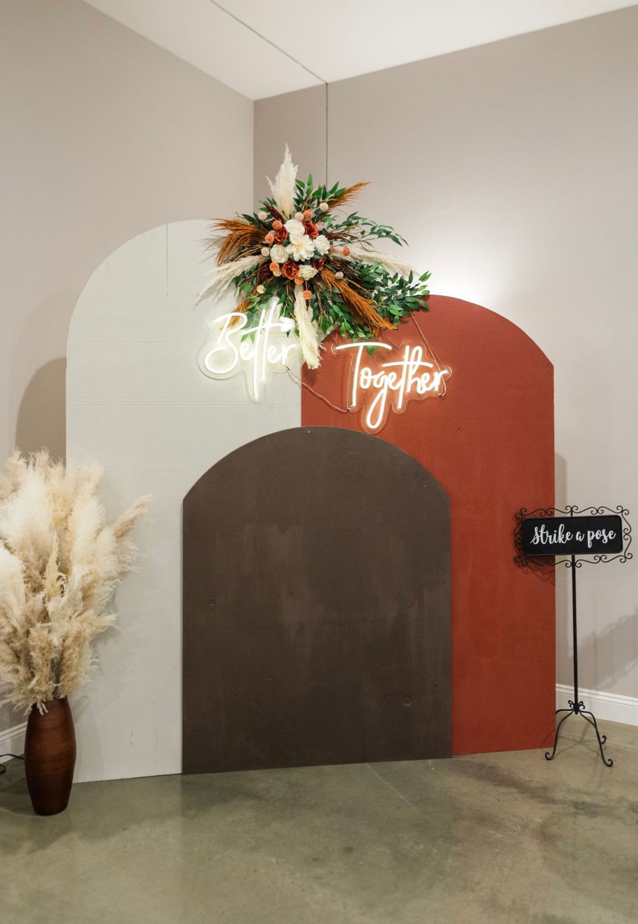 Decorative event backdrop with arches, flowers, neon sign, and a small chalkboard on a stand