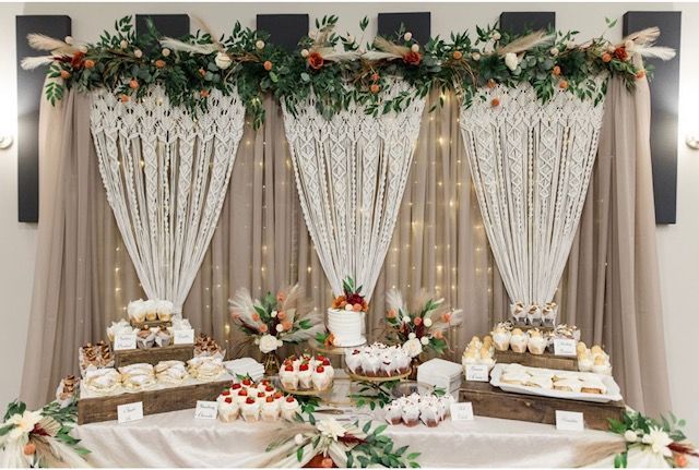Elegant dessert table with white drapes, greenery, fairy lights, and floral decorations