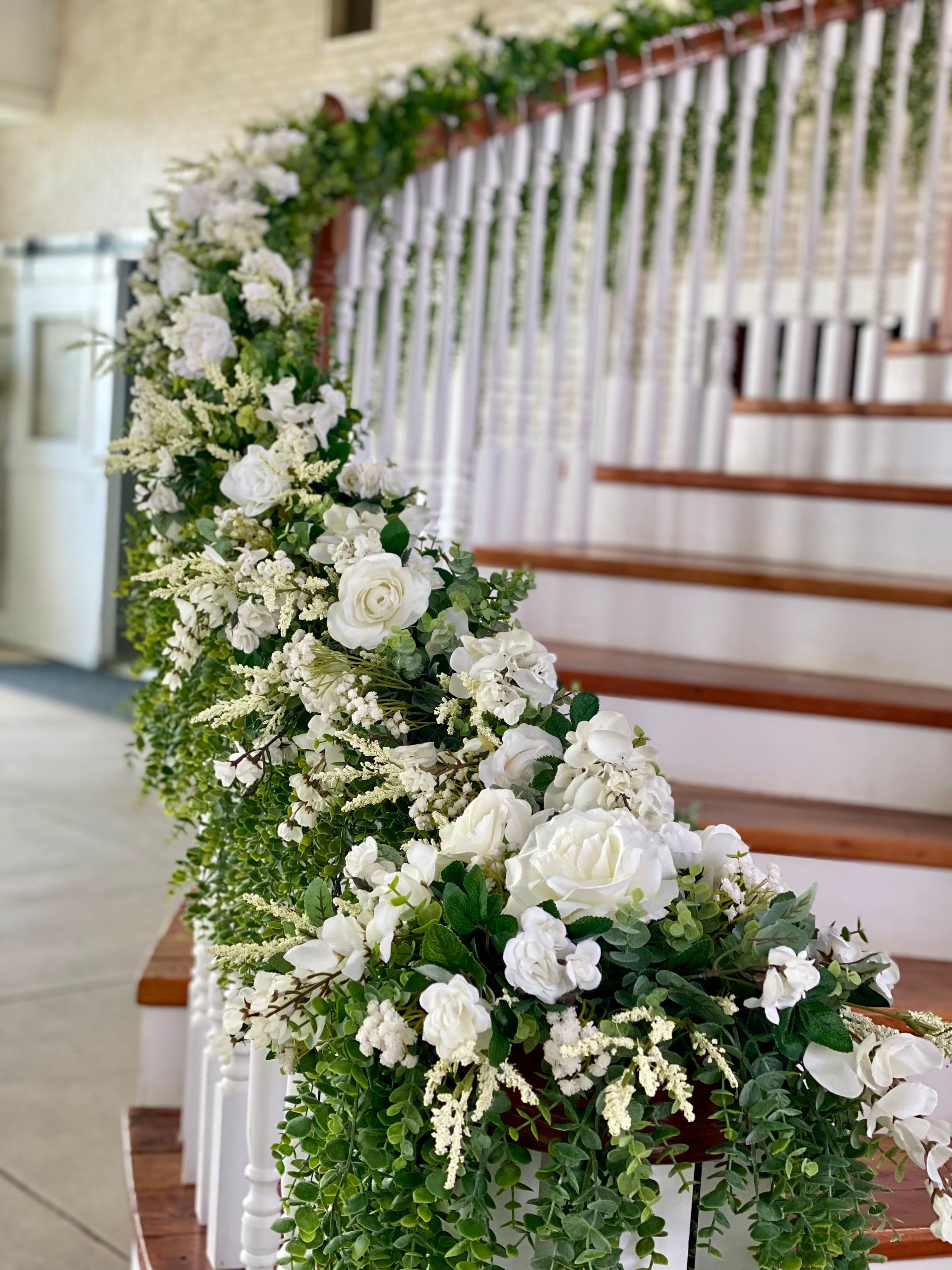 White floral garland draped along a staircase with white railings and wooden steps