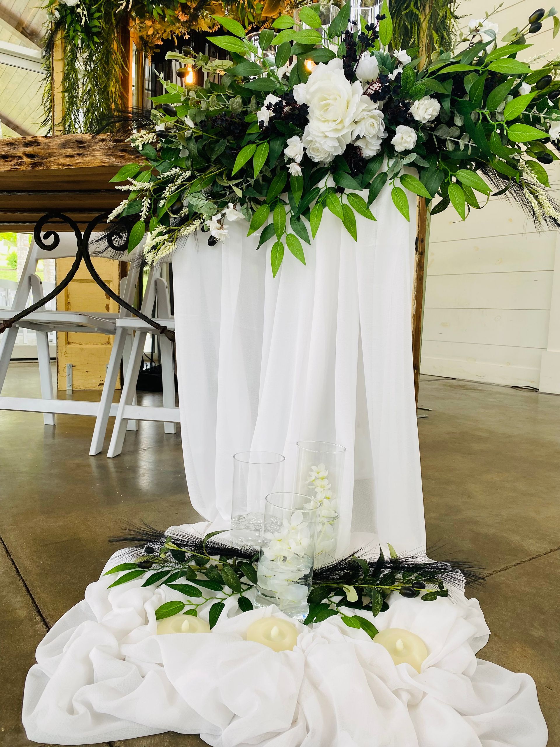 White floral wedding display with draped fabric and greenery in an indoor venue.