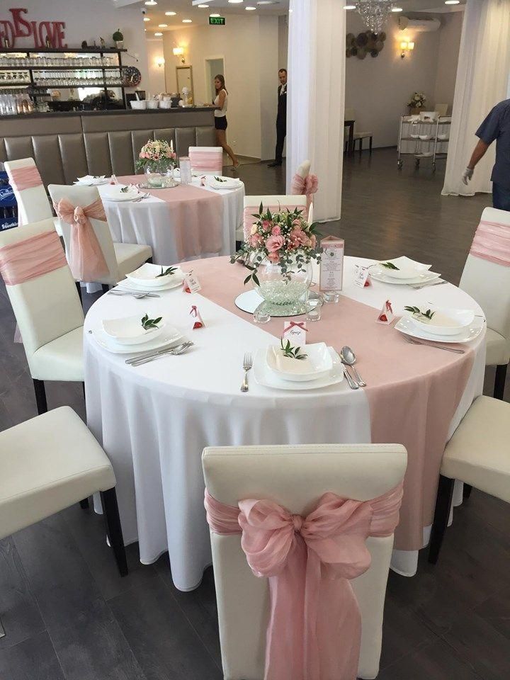 Round banquet tables with white linens, pink bows, and floral centerpieces in a decorated event hall