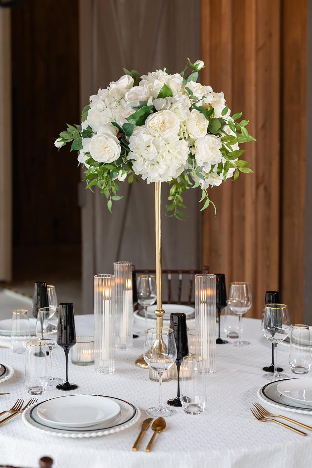 Elegant white floral centerpiece on a banquet table with glassware and gold accents
