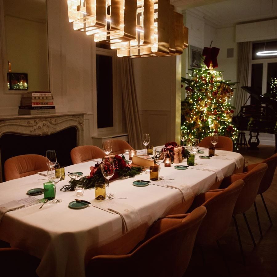 Elegant holiday dining room with a set table, warm chandelier light, and a decorated Christmas tree.