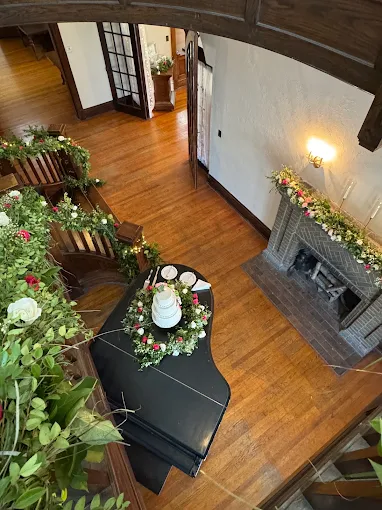 Overhead view of a wood-floored hallway with a black grand piano, plants, and a fireplace mantel