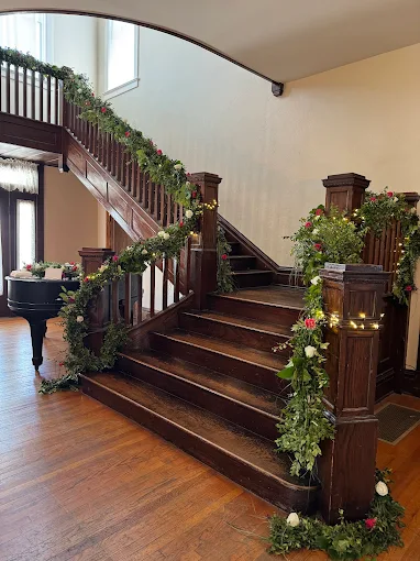 Grand staircase with dark wood railings, floral garlands, and warm hardwood flooring in a bright foyer