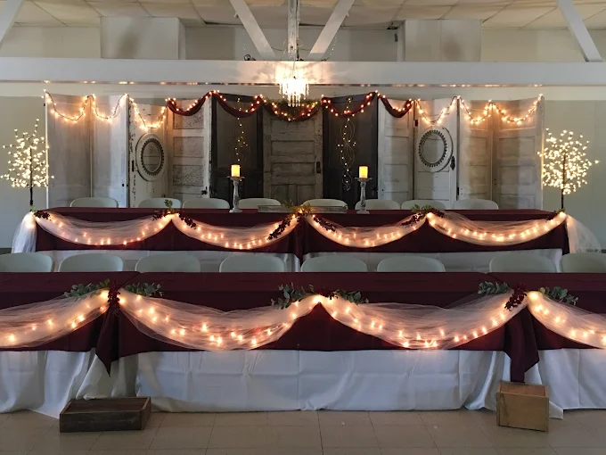 Decorated banquet table with string lights and draped burgundy-and-white tablecloths in a hall