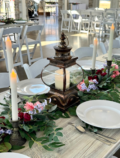 Elegant outdoor table setting with lantern centerpiece, candles, flowers, and white plates in a bright patio setting