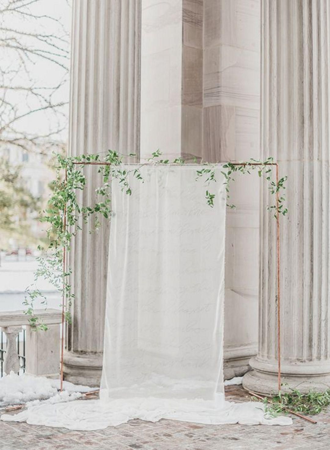 Sheer white drapes framed by tall stone columns and soft greenery outdoors
