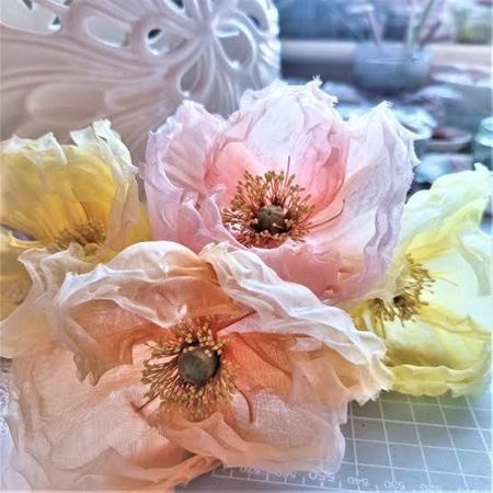 Pastel paper flowers in pink, peach, and yellow on a cutting mat