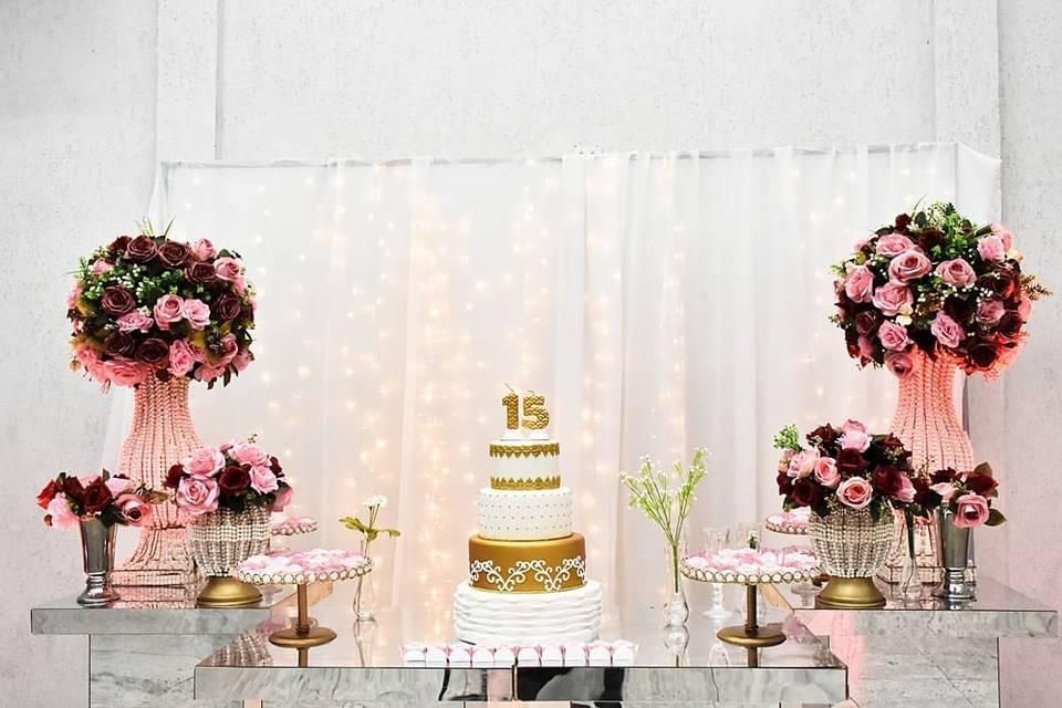 Elegant dessert table with a white-and-gold cake, pink floral arrangements, and twinkling lights.