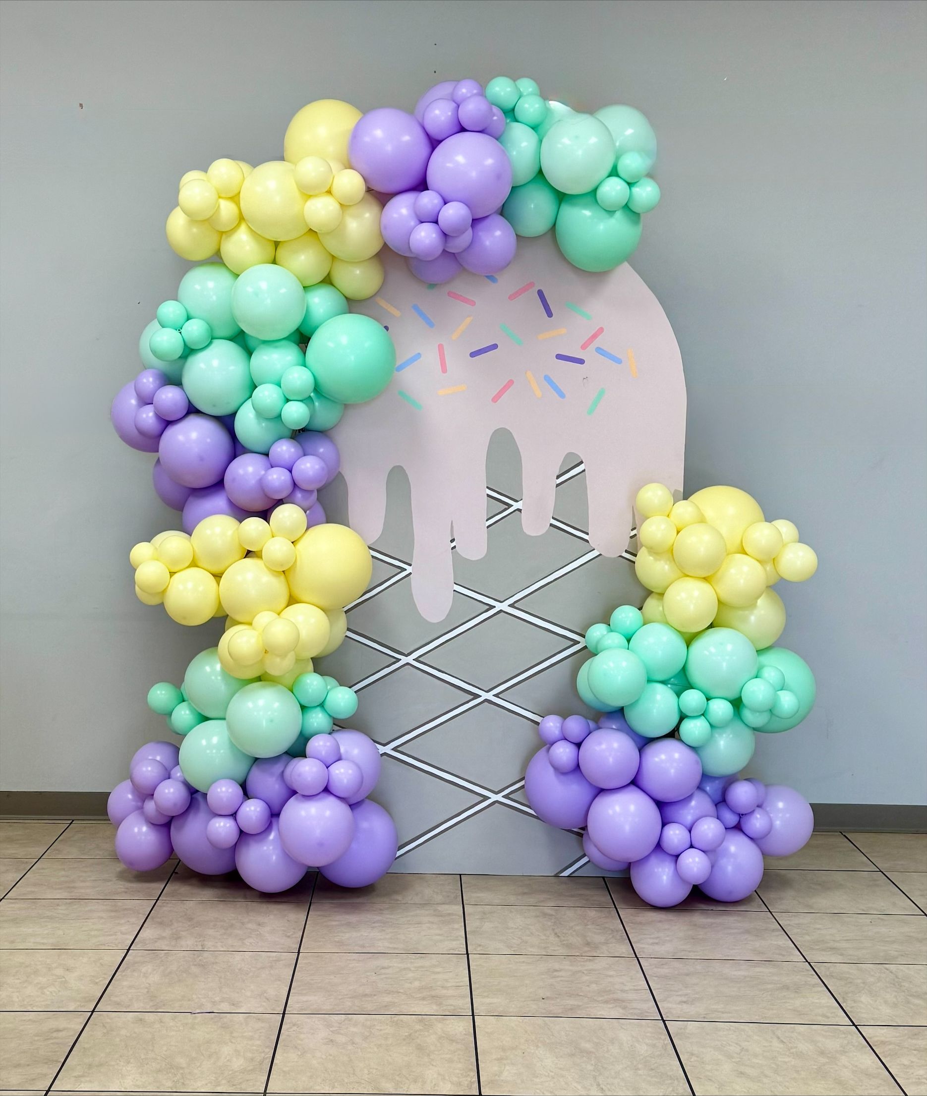 Pastel balloon arch framing a white cutout backdrop with confetti accents on a tiled floor