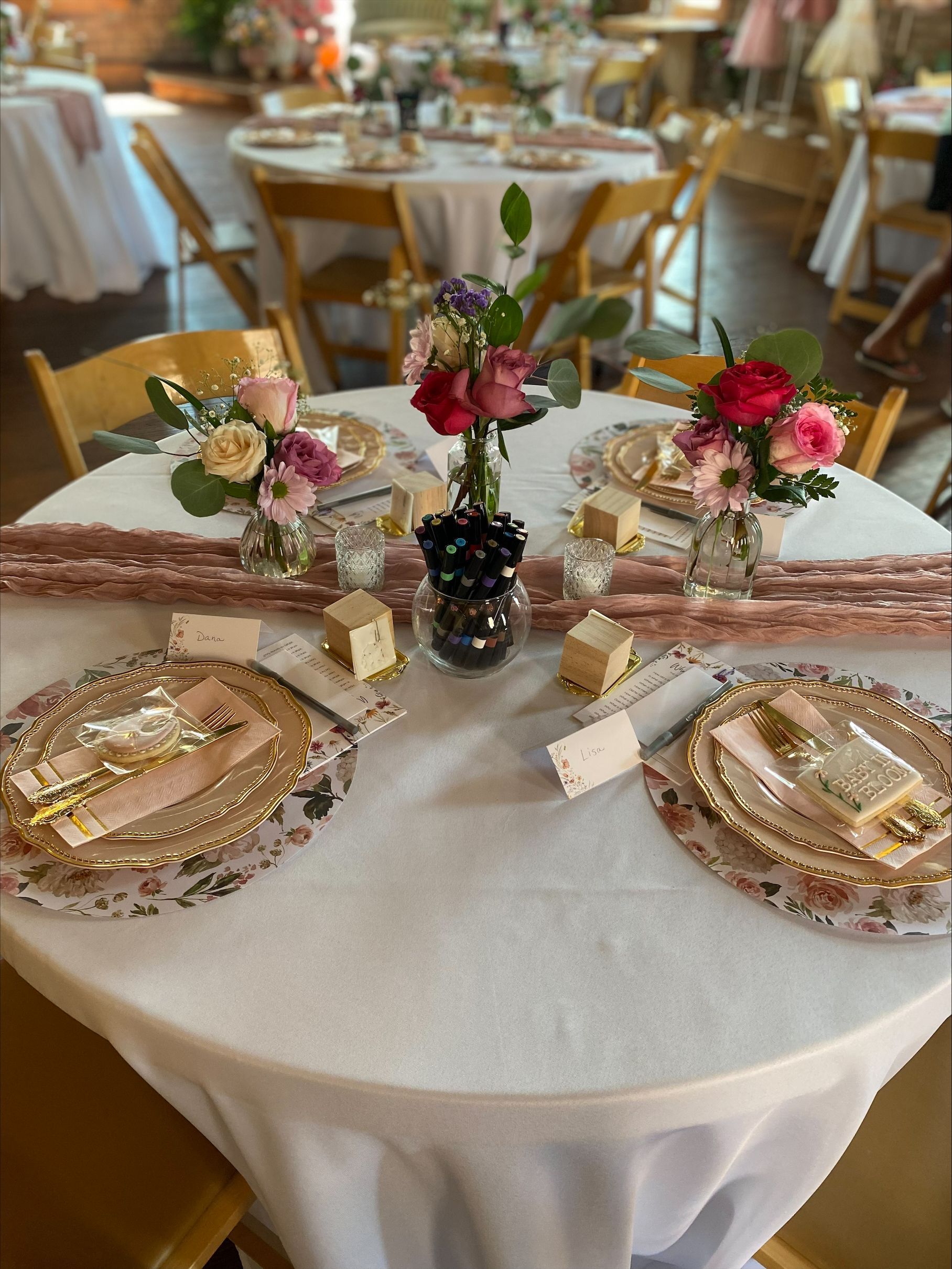 Round banquet table set with gold and pink floral tableware and a small centerpiece in a softly lit event hall