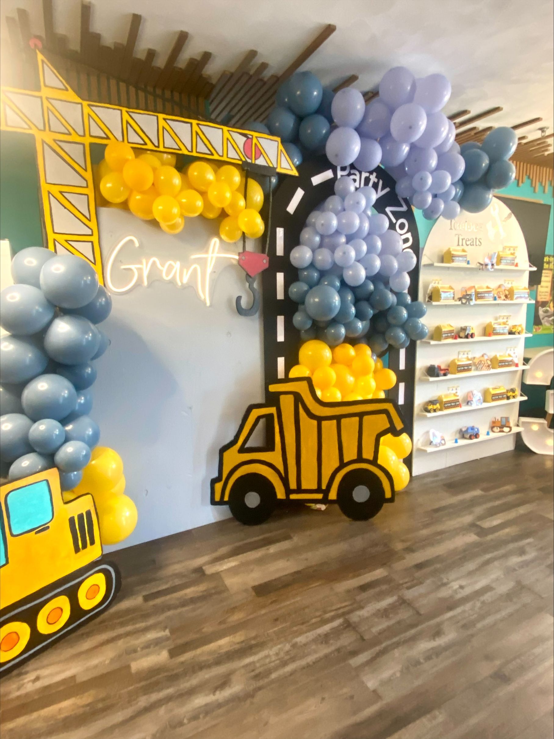 Construction-themed balloon backdrop with yellow dump truck, blue balloon columns, and “Grant” sign