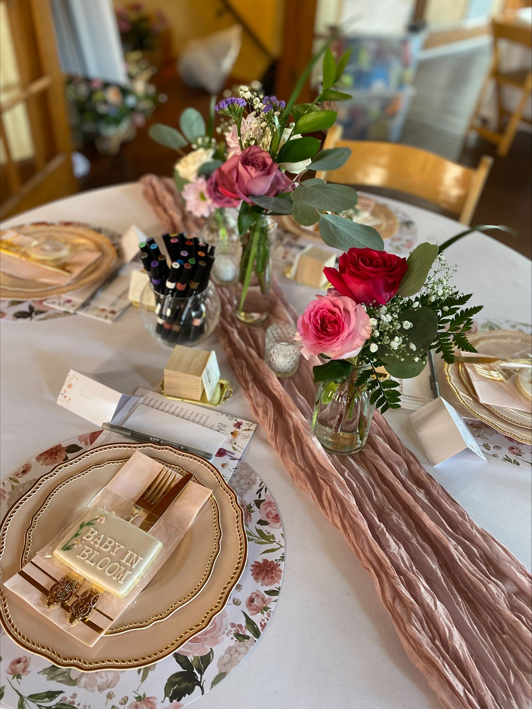 Elegant table setting with pink flowers, gold plates, and a white iced dessert bar centerpiece