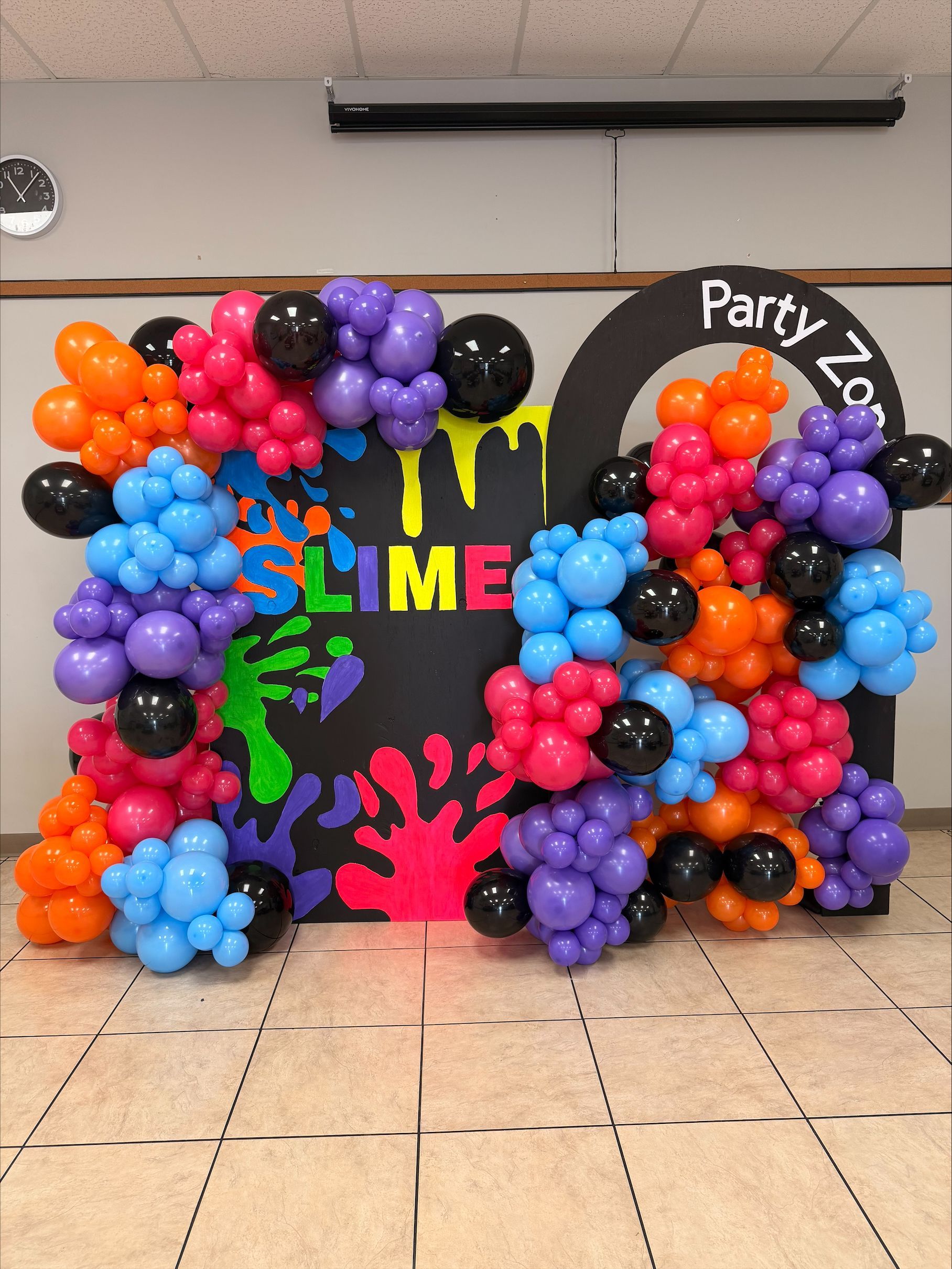 Colorful balloon arch and clusters framing a “Party to SLIME” backdrop in an indoor event space