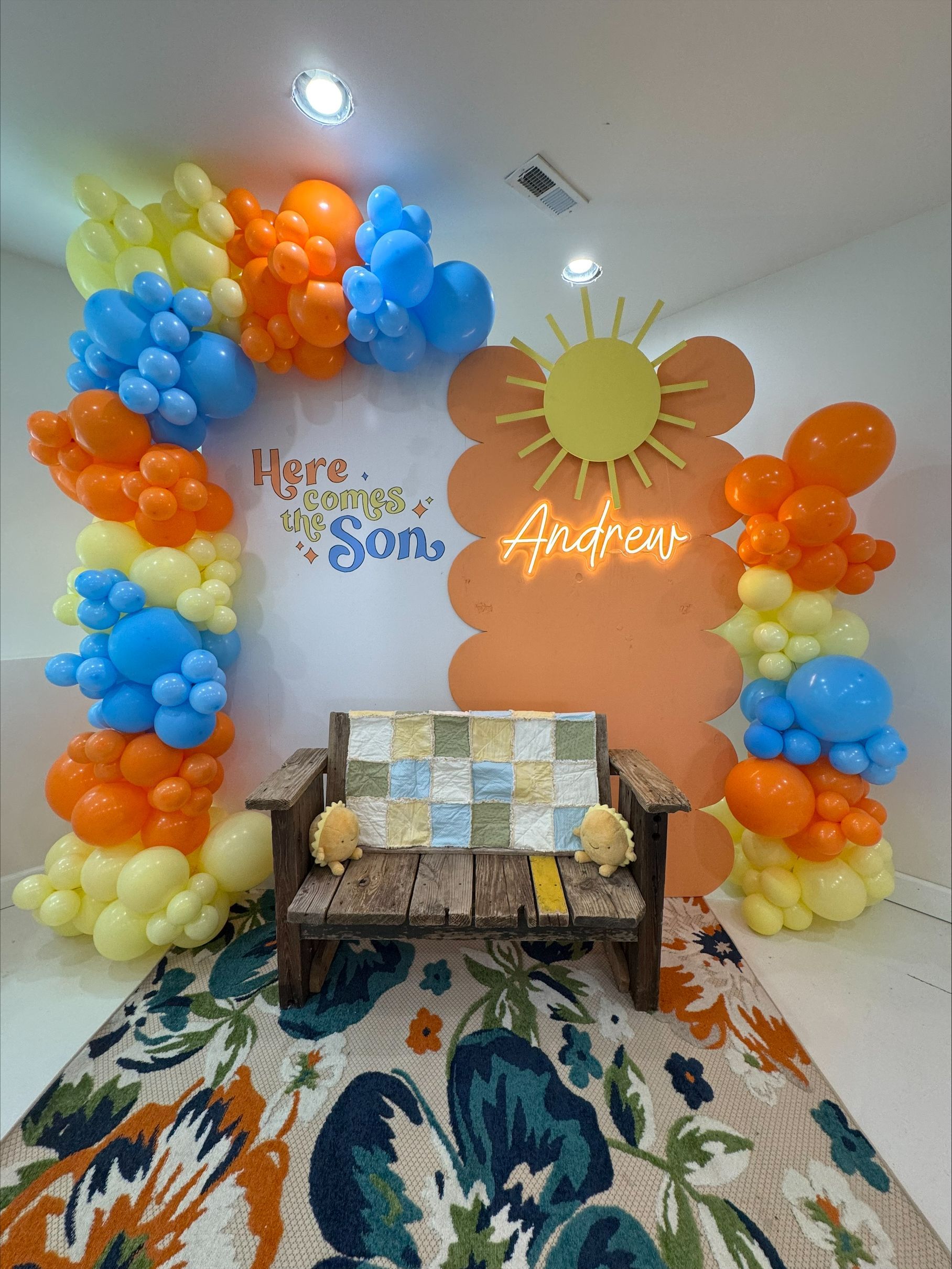 Colorful balloon arch framing a couch and sun backdrop in a decorated party room