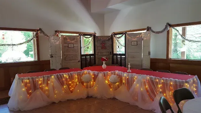 Decorated banquet table with white and red drapes, string lights, and garlands in a hall