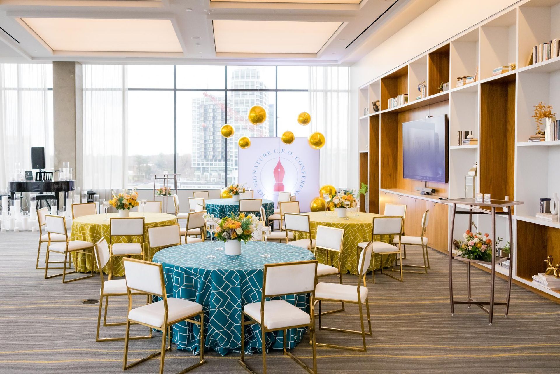 Bright event hall with round tables, gold chairs, and yellow balloon decorations.